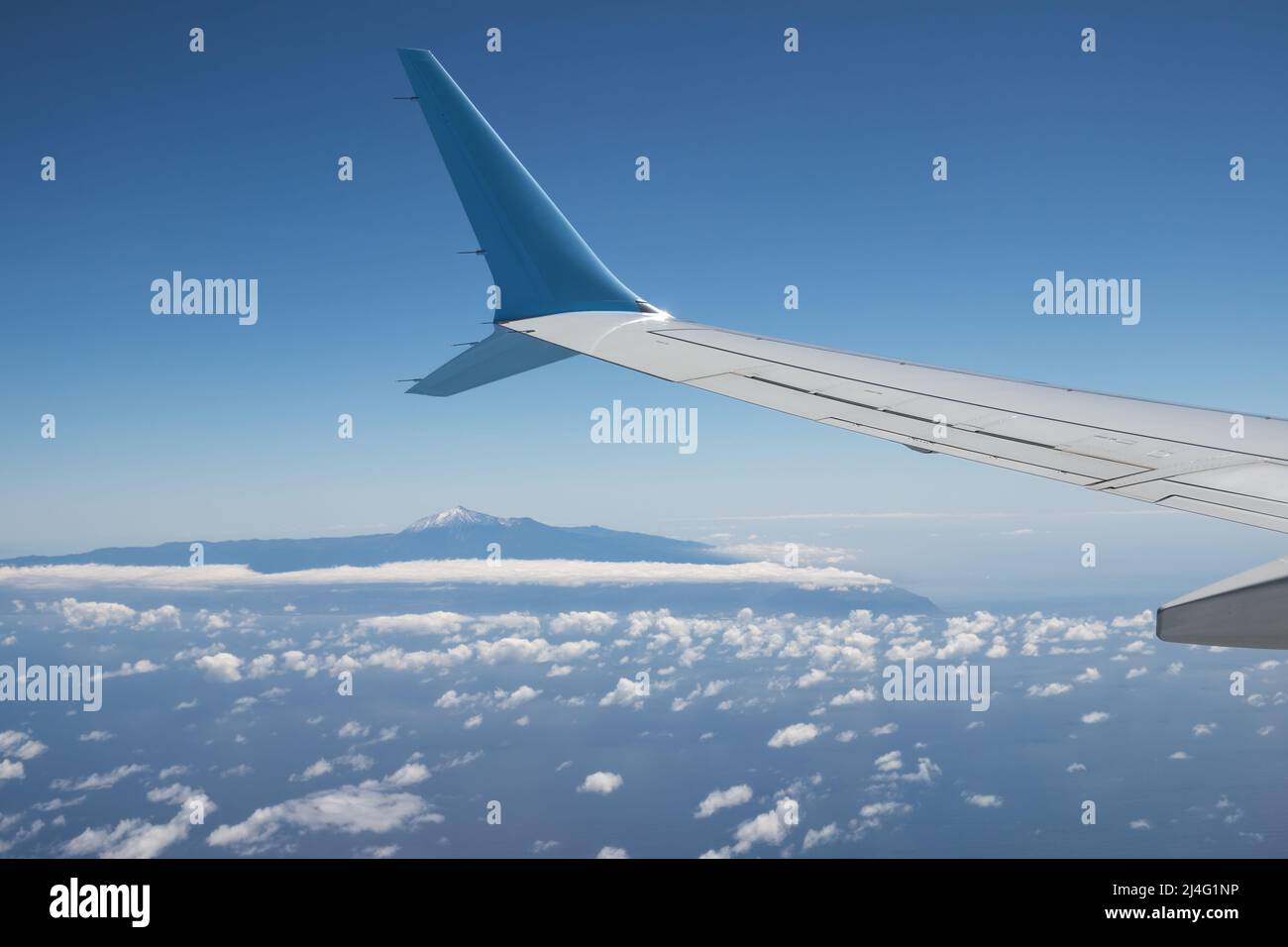 Wing of an airplane flying above Atlantic Ocean with view at island Tenerife with mount teide Stock Photo