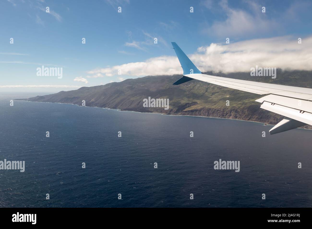 Wing of an airplane flying above Atlantic Ocean approaching Canary Island La Palma Stock Photo