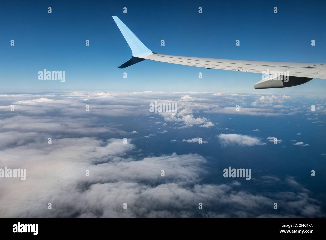 Wing of an airplane flying above the Atlantic Ocean with view at white clouds Stock Photo