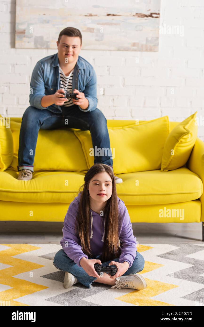 KYIV, UKRAINE - JANUARY 21, 2022: Teen girl with down syndrome playing video game with blurred friend at home Stock Photo