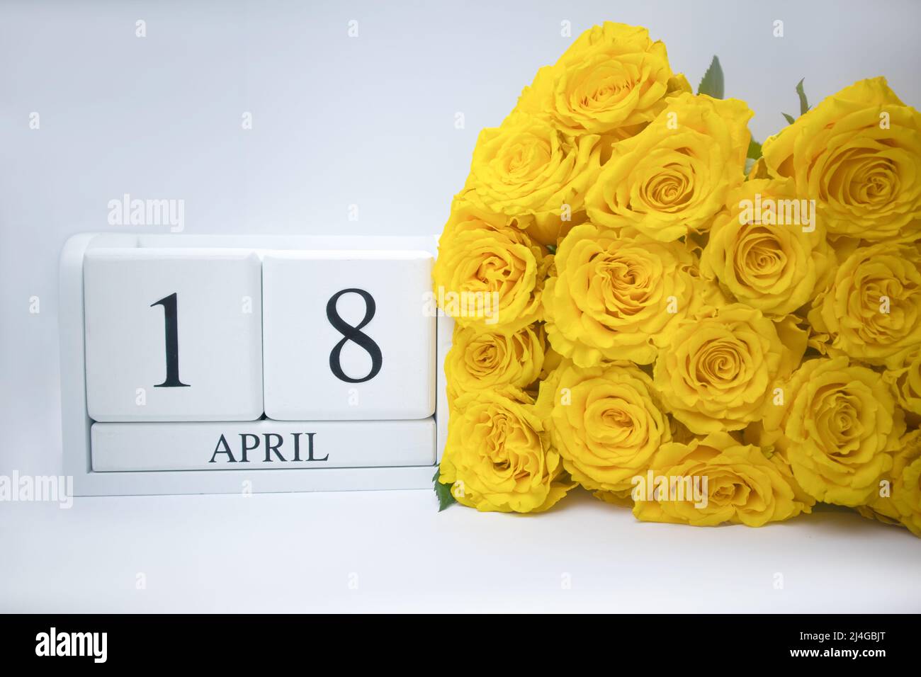 April 18 on a white, wooden calendar, next to a bouquet of yellow roses. Stock Photo