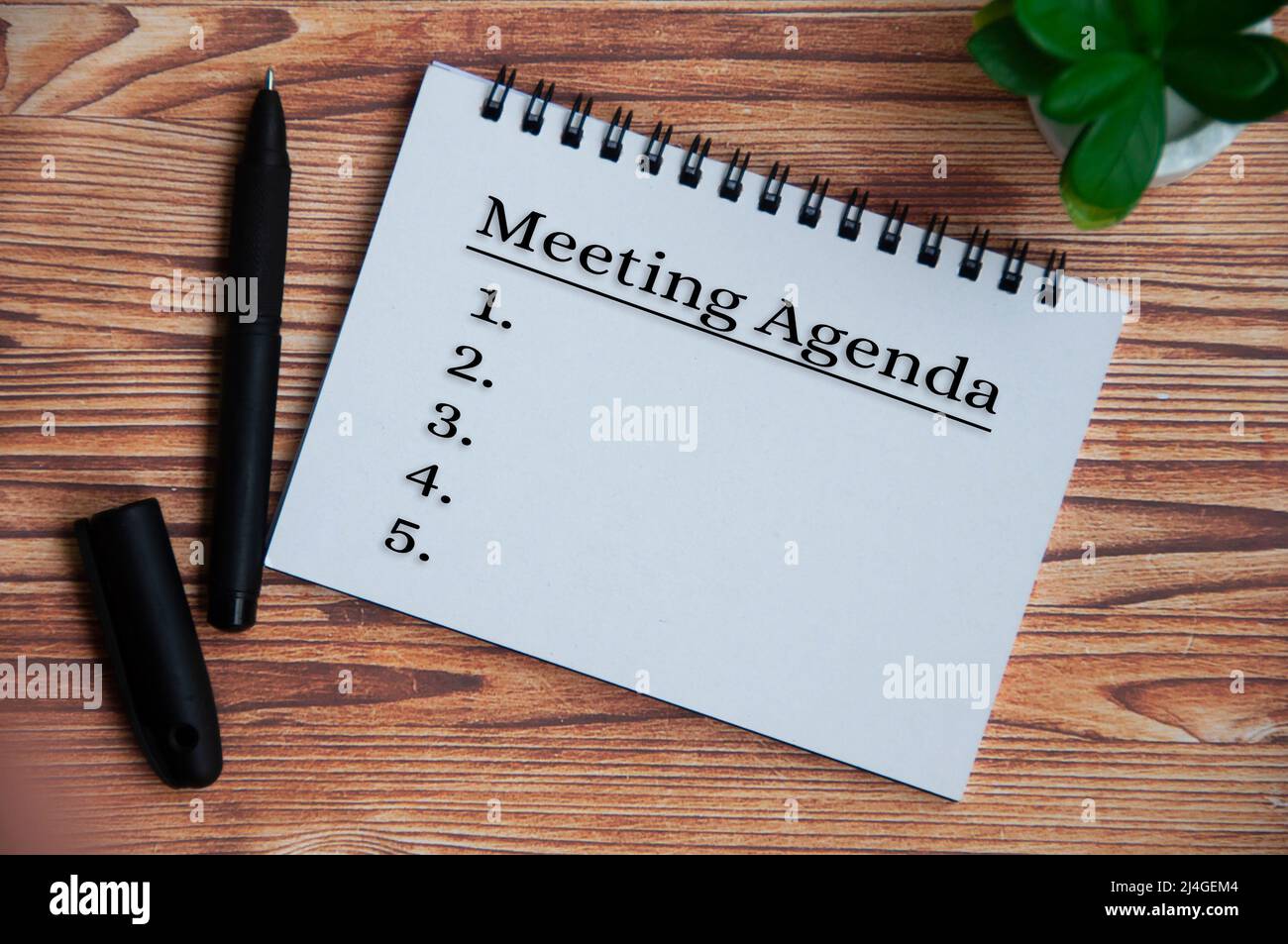 Meeting agenda text on notepad with plant, pen and wooden table background. Meeting concept Stock Photo