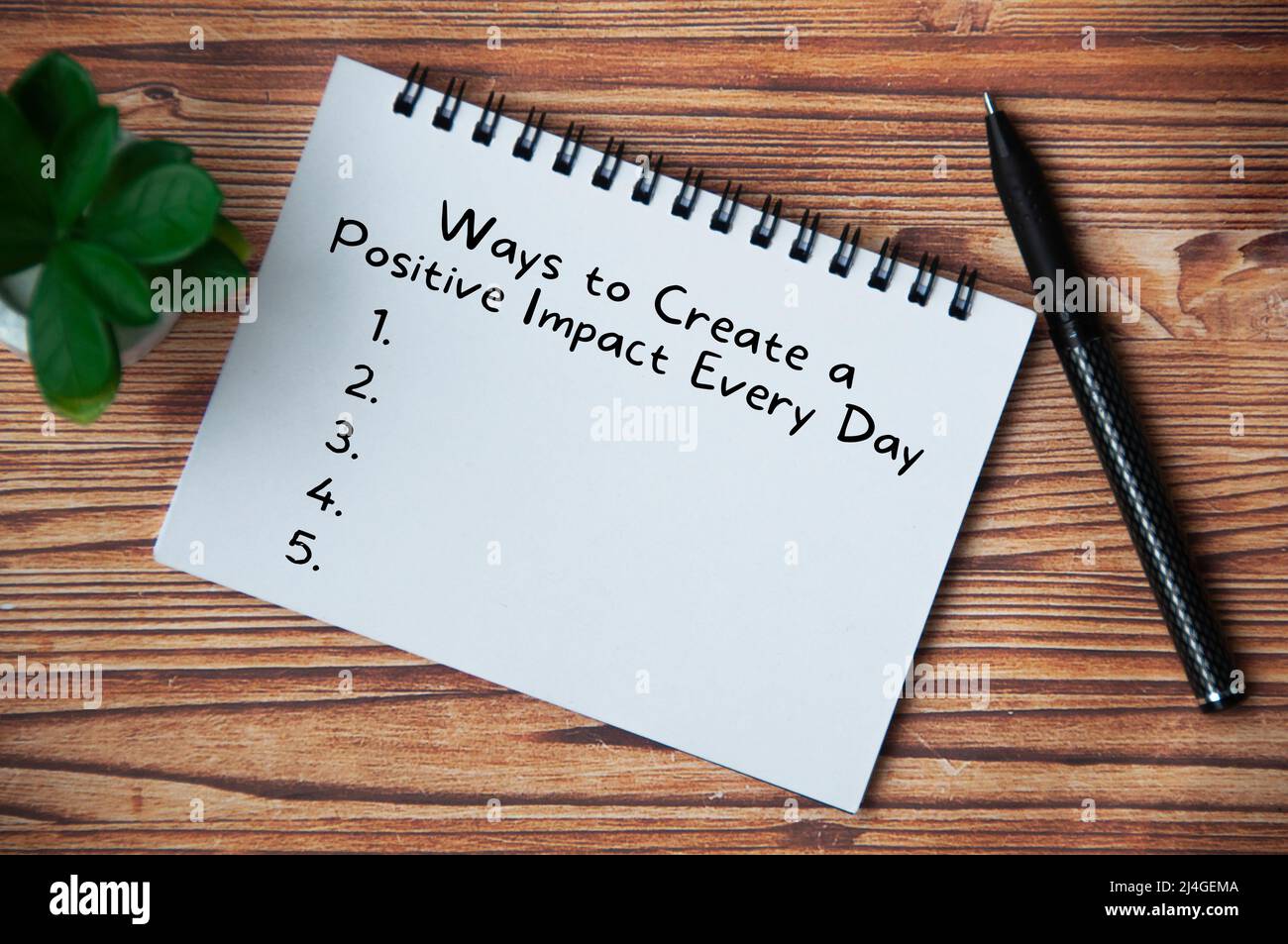 Top view of text - Ways to create a positive impact every day. With pen and plant on wooden table. Stock Photo