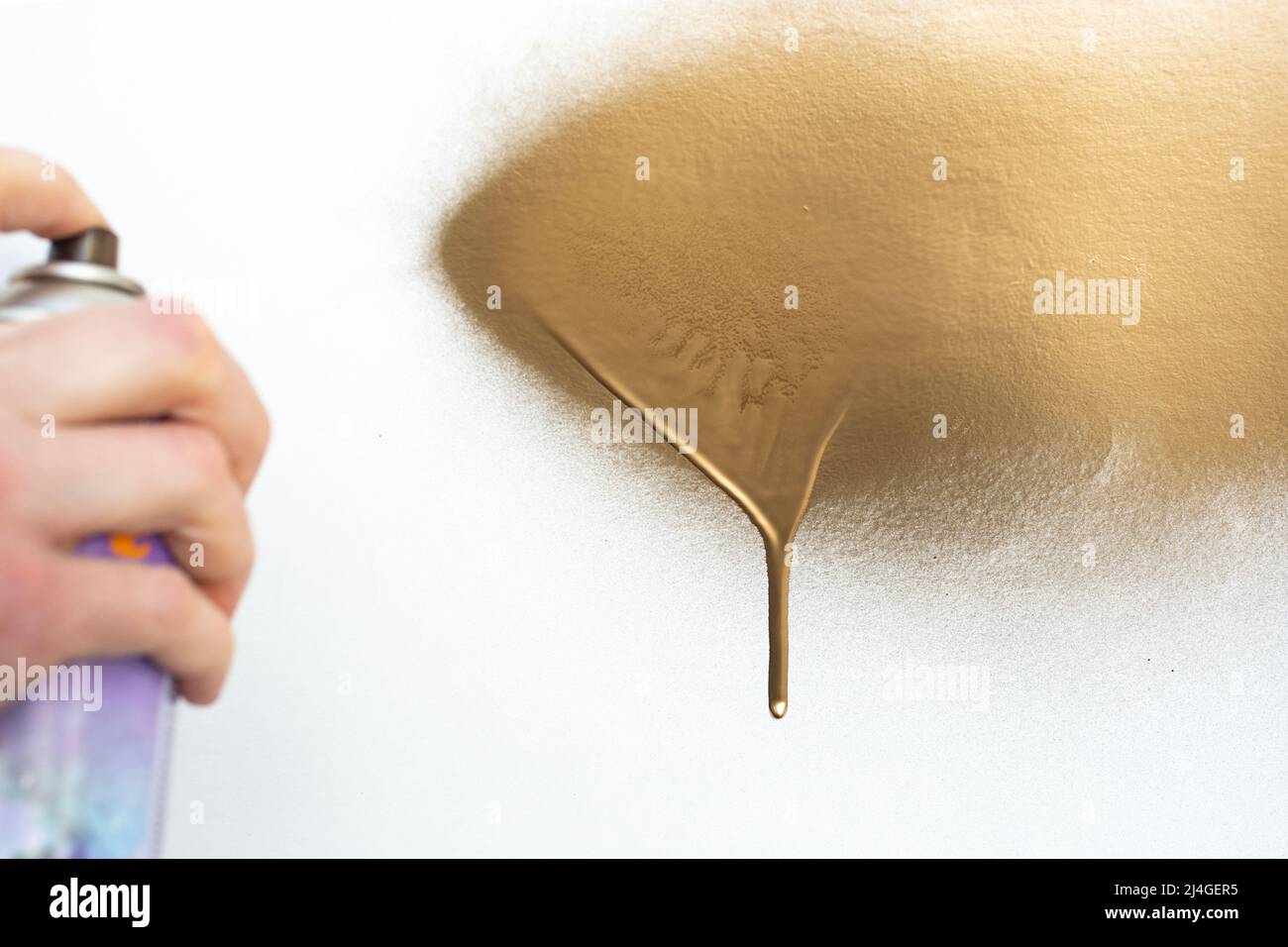 blurred hand holding a golden paint spray can, painting a white surface Stock Photo