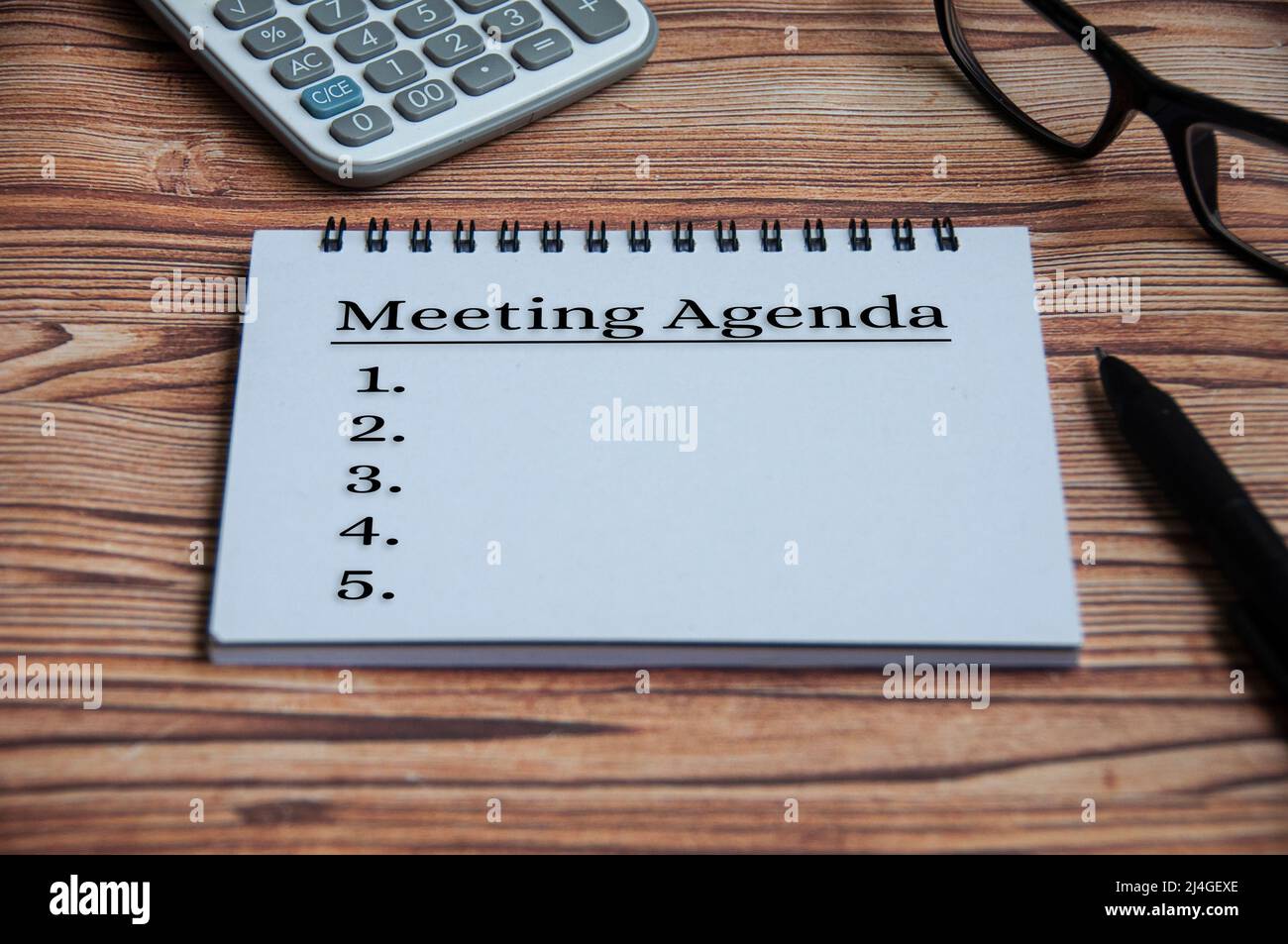 Meeting agenda text on notepad with calculator, pen, glasses and wooden table background. Meeting concept Stock Photo