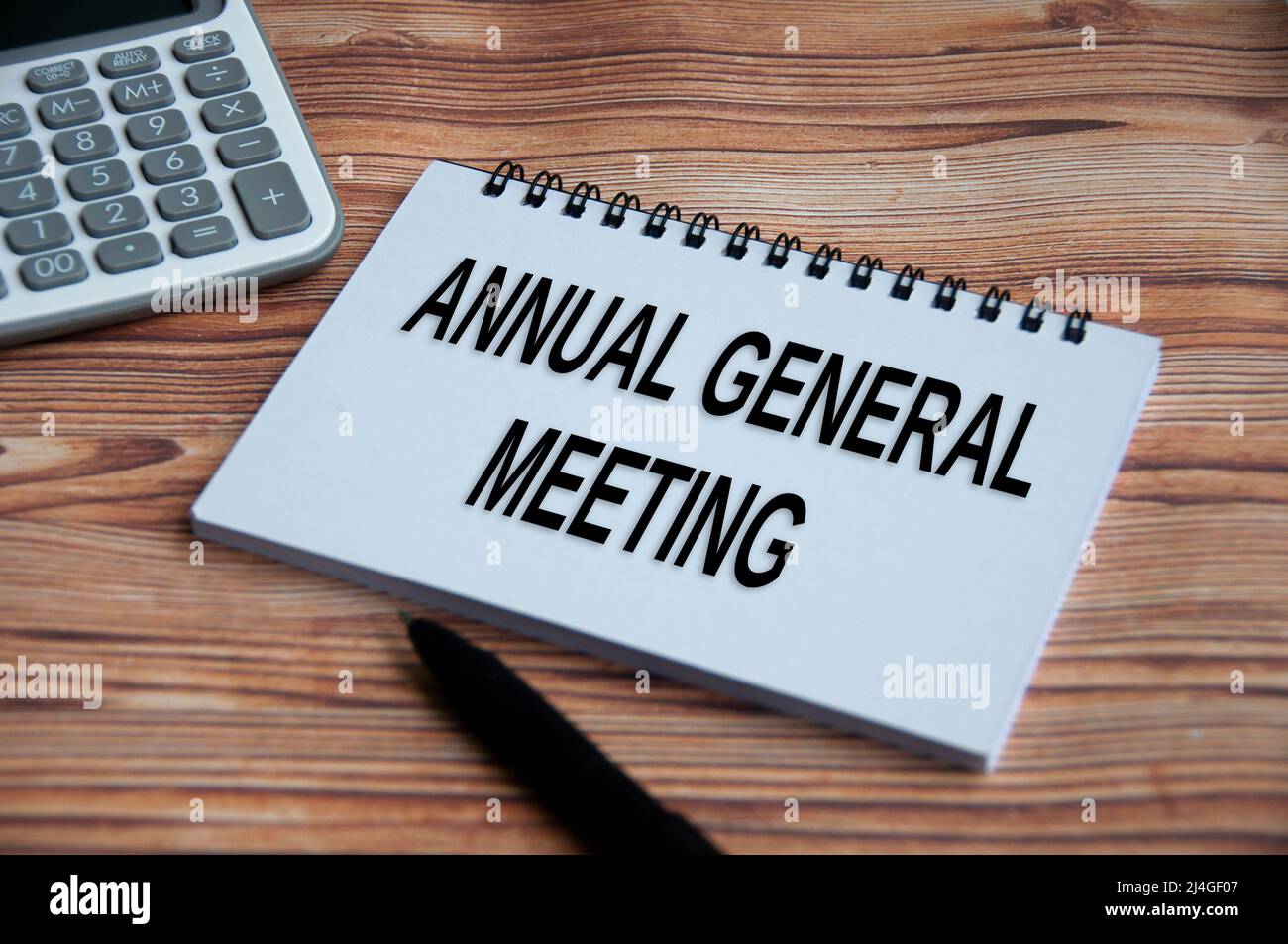 Annual general meeting text on notepad with calculator, pen and wooden table background. Business concept Stock Photo