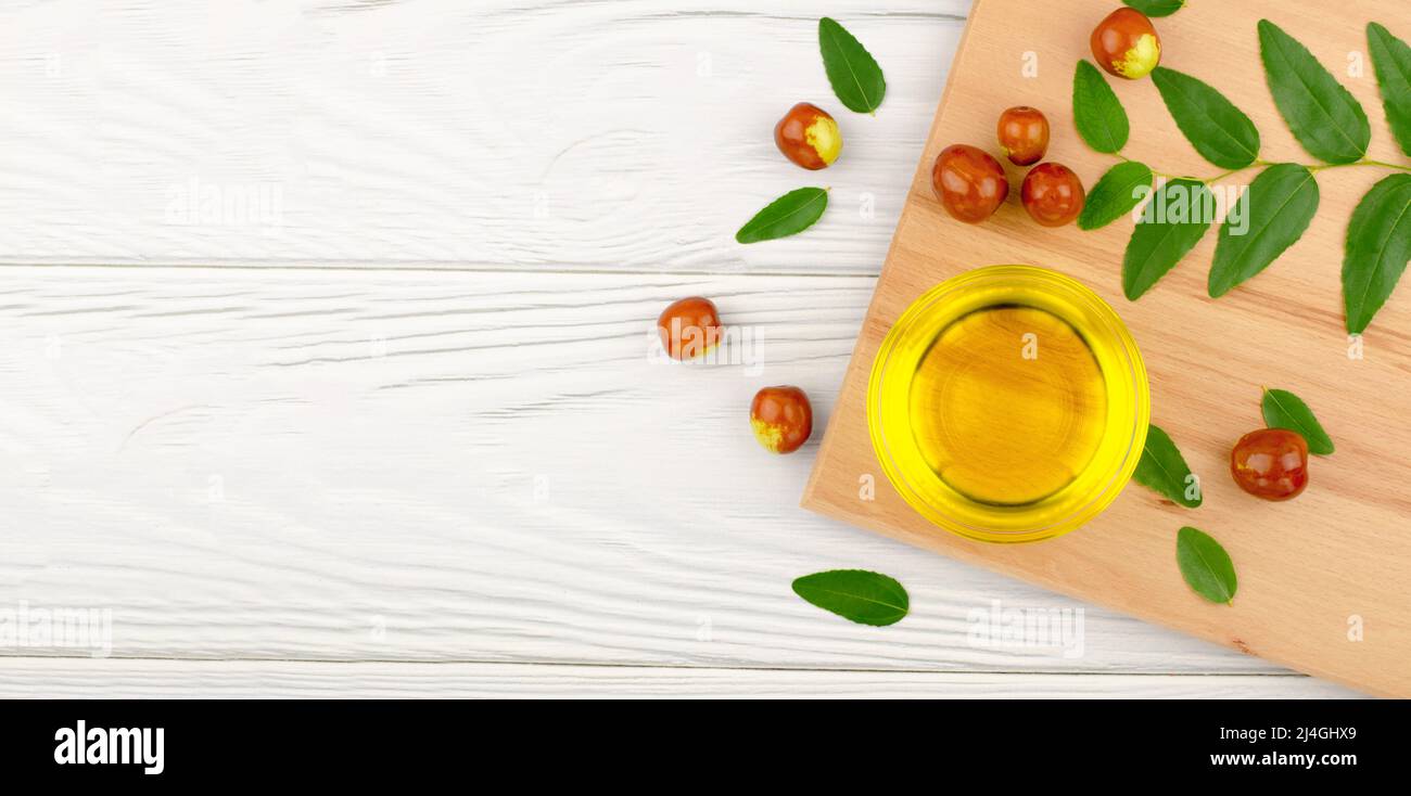 Fresh ripe jojoba fruit and jojoba oil in bowl on wooden table, banner Stock Photo