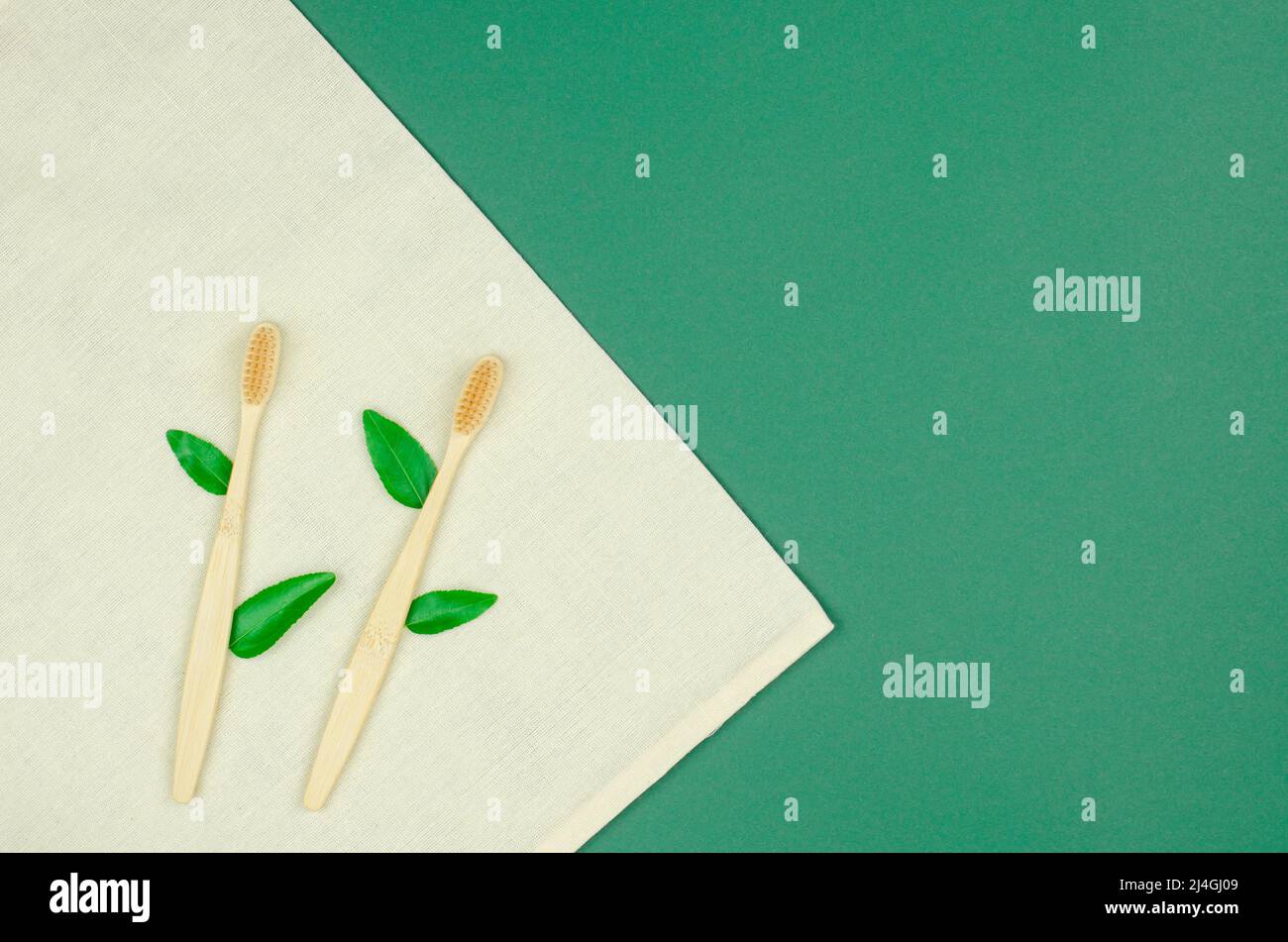 Bamboo toothbrushes with green leaves lie on a linen material. Eco ...