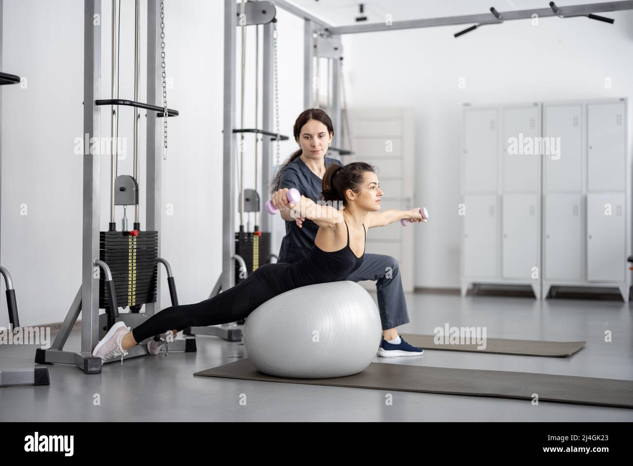 Woman doing exercises on fitness ball and dumbbells with rehabilitation specialist at the gym Stock Photo