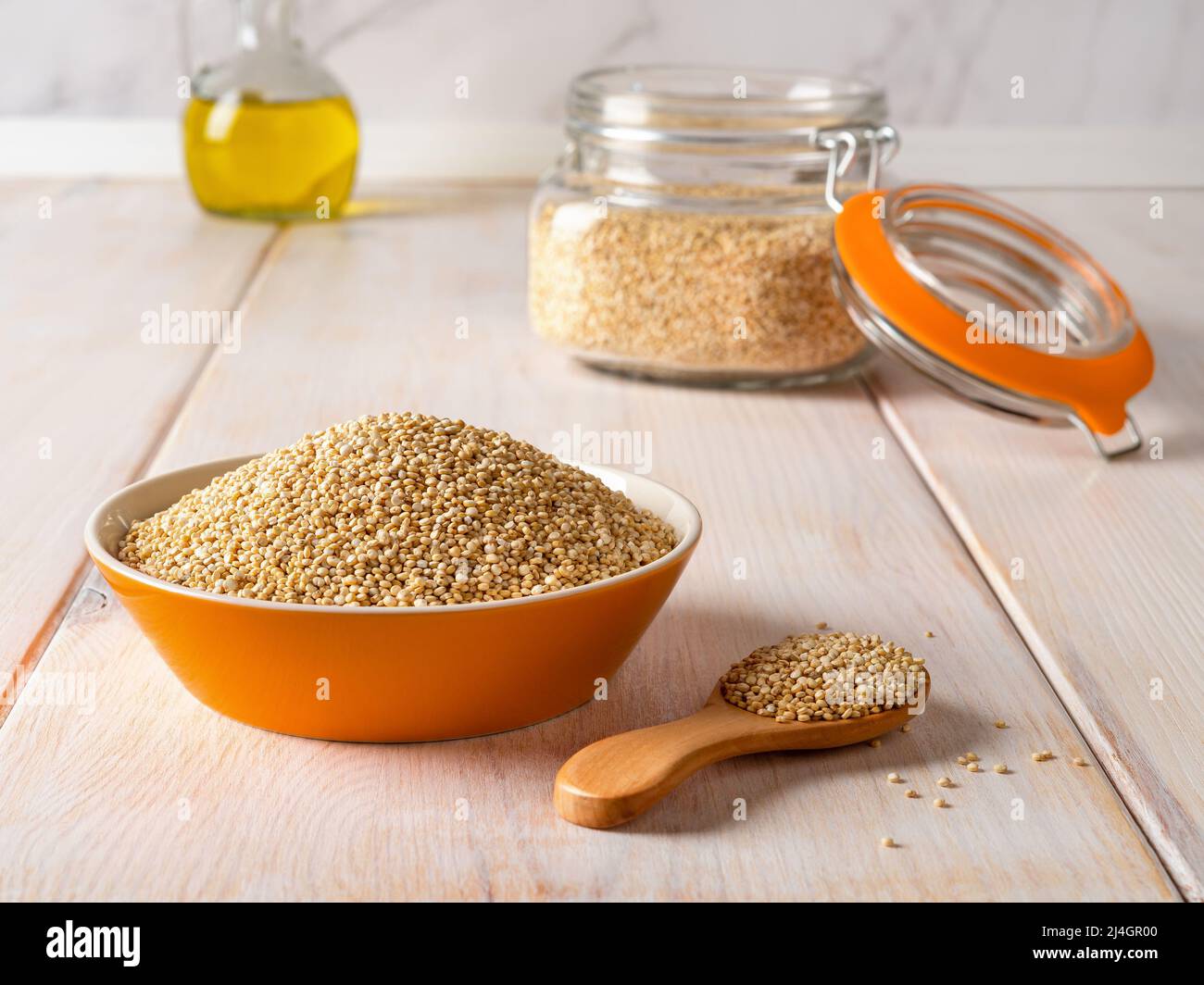 Raw white quinoa seeds in a bowl, wooden spoon and clip top glass jar on a white rustic table. Ingredient of gluten free dishes. Chenopodium quinoa. Stock Photo