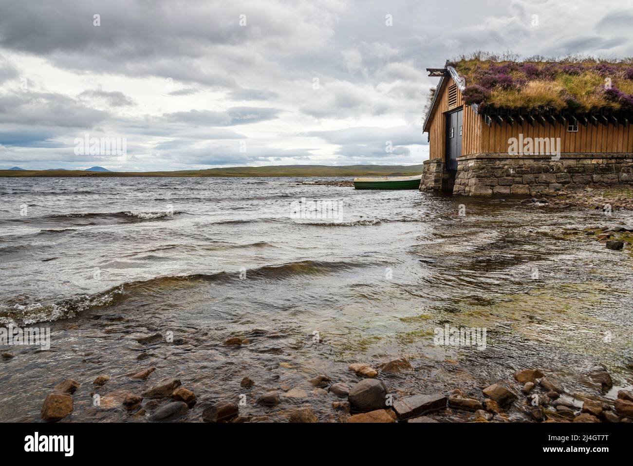 A wooden boathouse with a turf roof beside Loch Loyal on a cloudy day. Stock Photo
