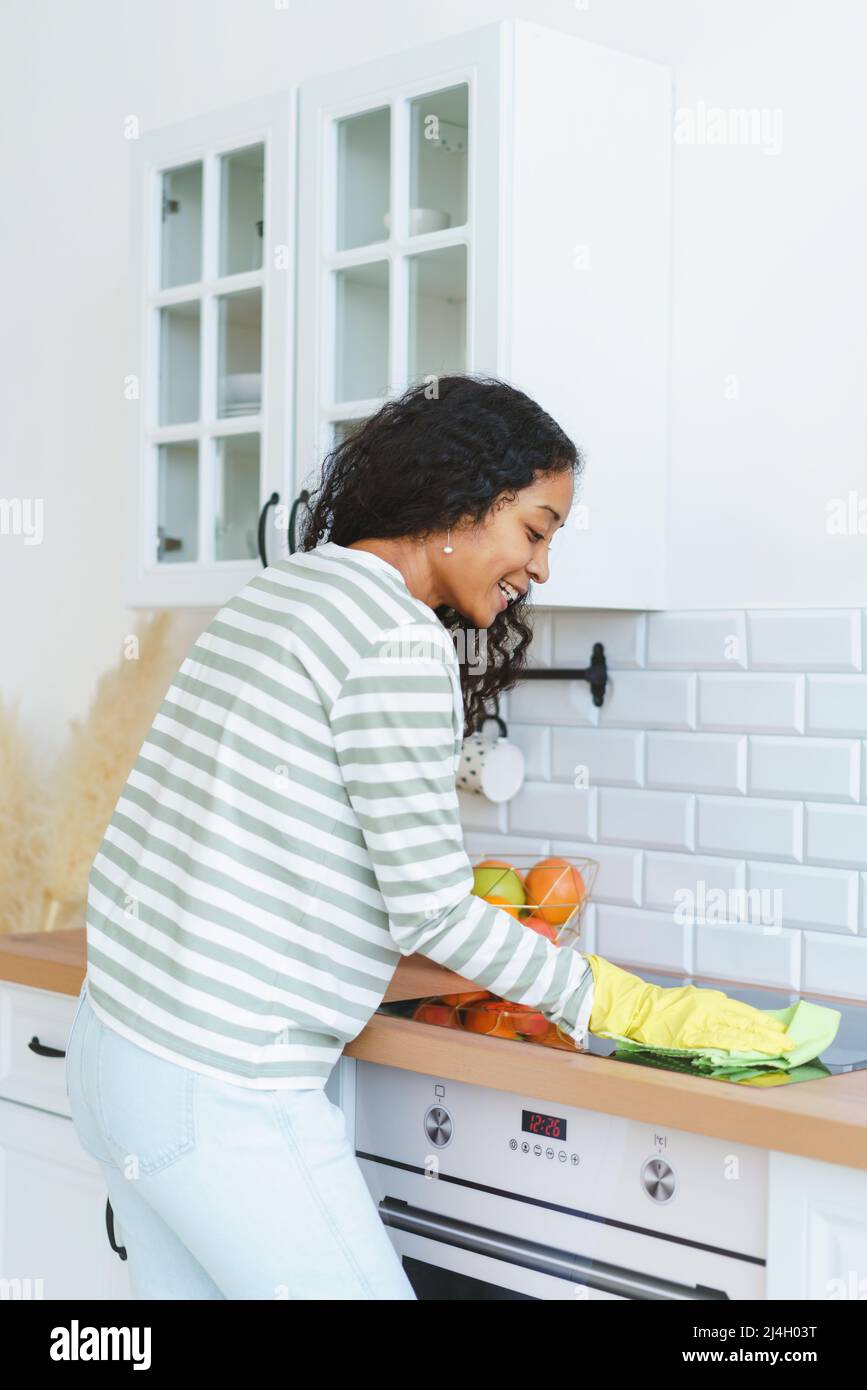 Back view of AfricanAmerican female cleaning induction stove in rubber