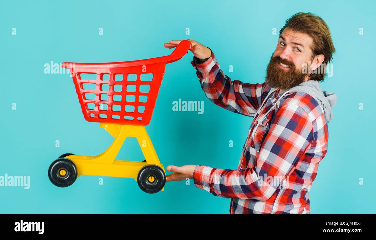 Smiling bearded man with empty shopping cart. Buyer in supermarket. Buying products. Sale. Discount. Stock Photo