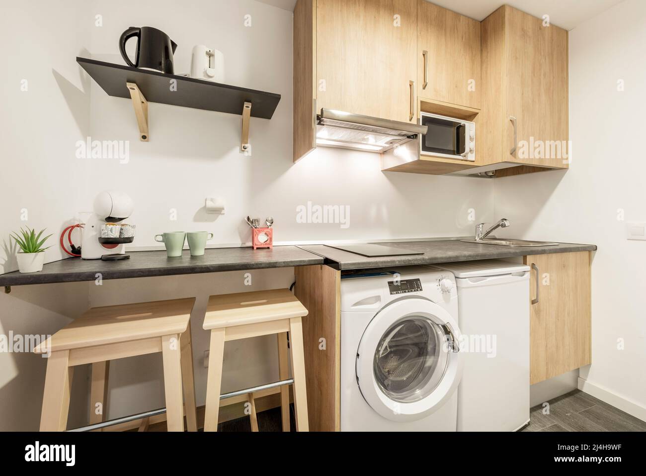 https://c8.alamy.com/comp/2J4H9WF/kitchen-with-dark-gray-wooden-countertops-with-a-coffee-maker-and-mugs-on-it-light-wooden-cabinets-and-white-appliances-2J4H9WF.jpg