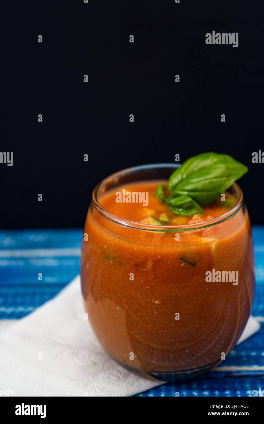 Important Glass with the refreshing Andalusian Gazpacho on a blue wooden table. Cold vegetable and organic soup or drink that is drunk in summer or ho Stock Photo