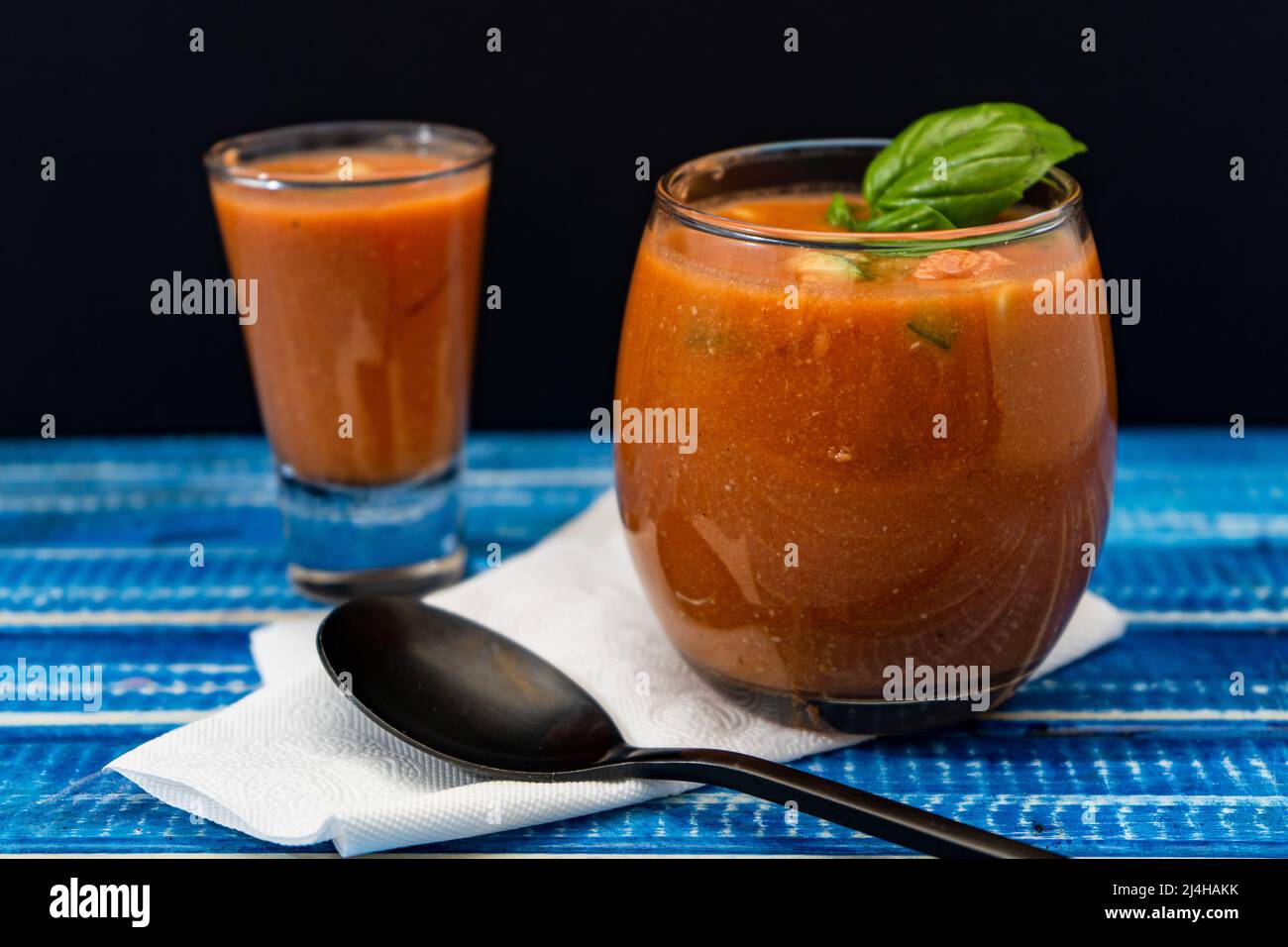 Important Glass and a shot, both with the refreshing Andalusian Gazpacho on a blue wooden table. Cold vegetable and organic soup or drink that is drun Stock Photo