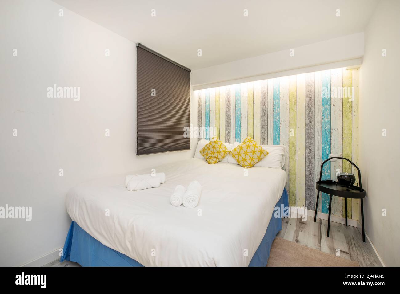 Double bed against the wall, window with black shutter, wall with