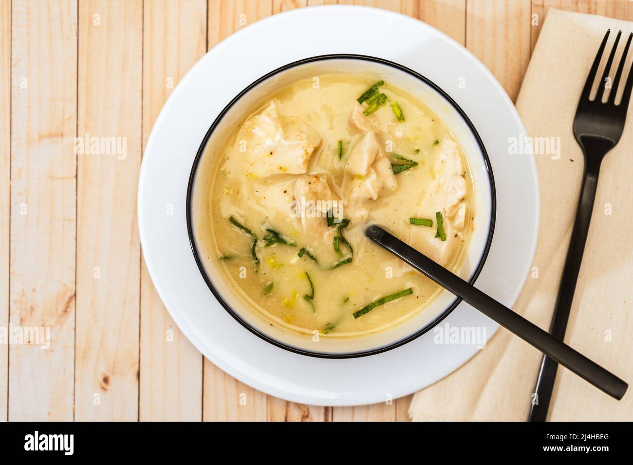 Modern bowl with a traditional homemade cream of poultry soup with chicken pieces, parsley and cream on a rustic or country style wooden table. Natura Stock Photo