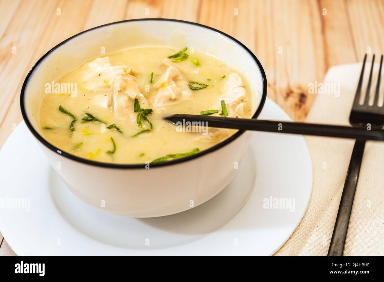 Modern bowl with a traditional homemade cream of poultry soup with chicken pieces, parsley and cream on a rustic or country style wooden table. Natura Stock Photo
