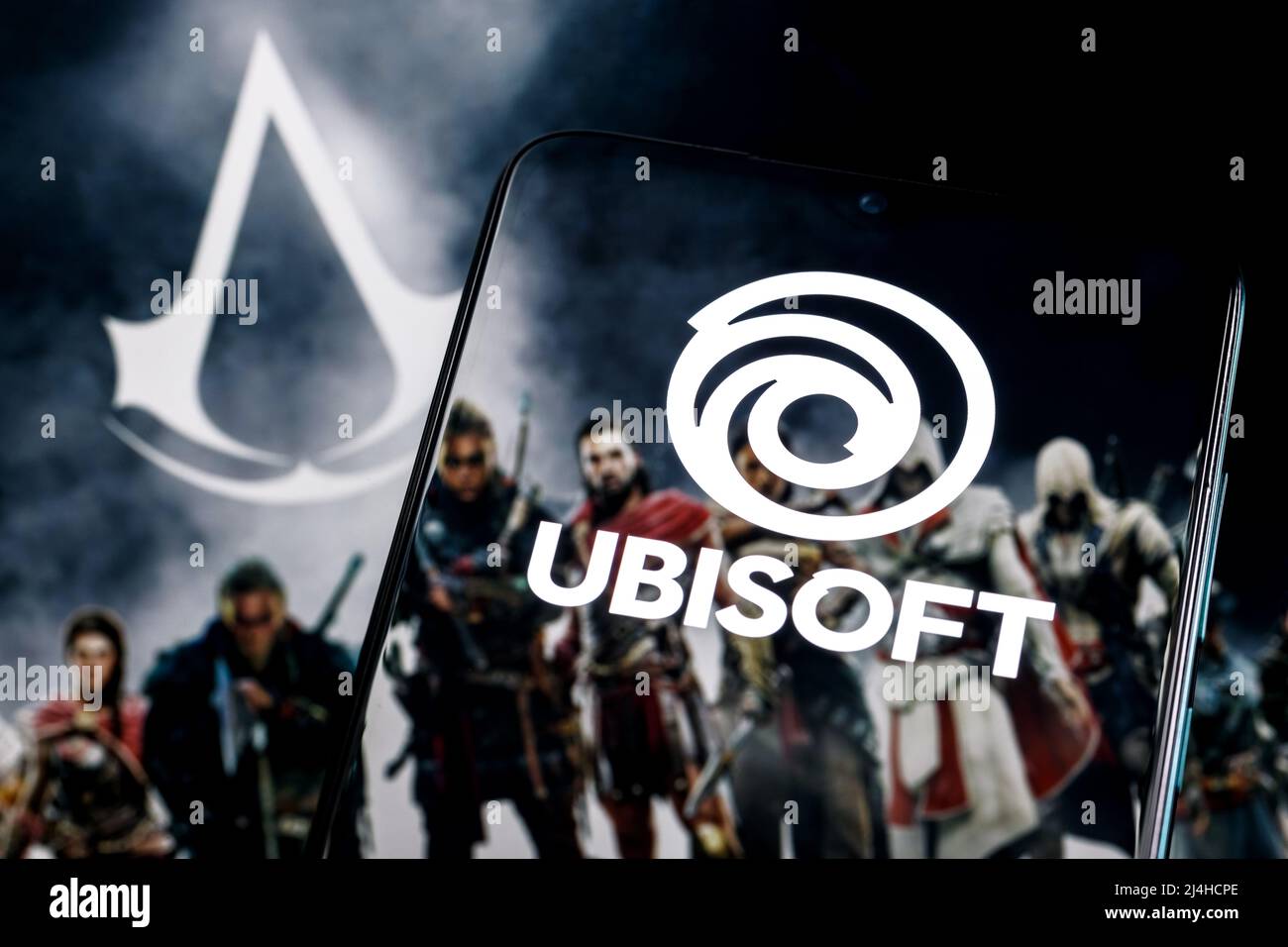 Ubisoft is French video game company. Ubisoft logo on smartphone screen. Frame from Assassin Creed franchise game on background. Stock Photo