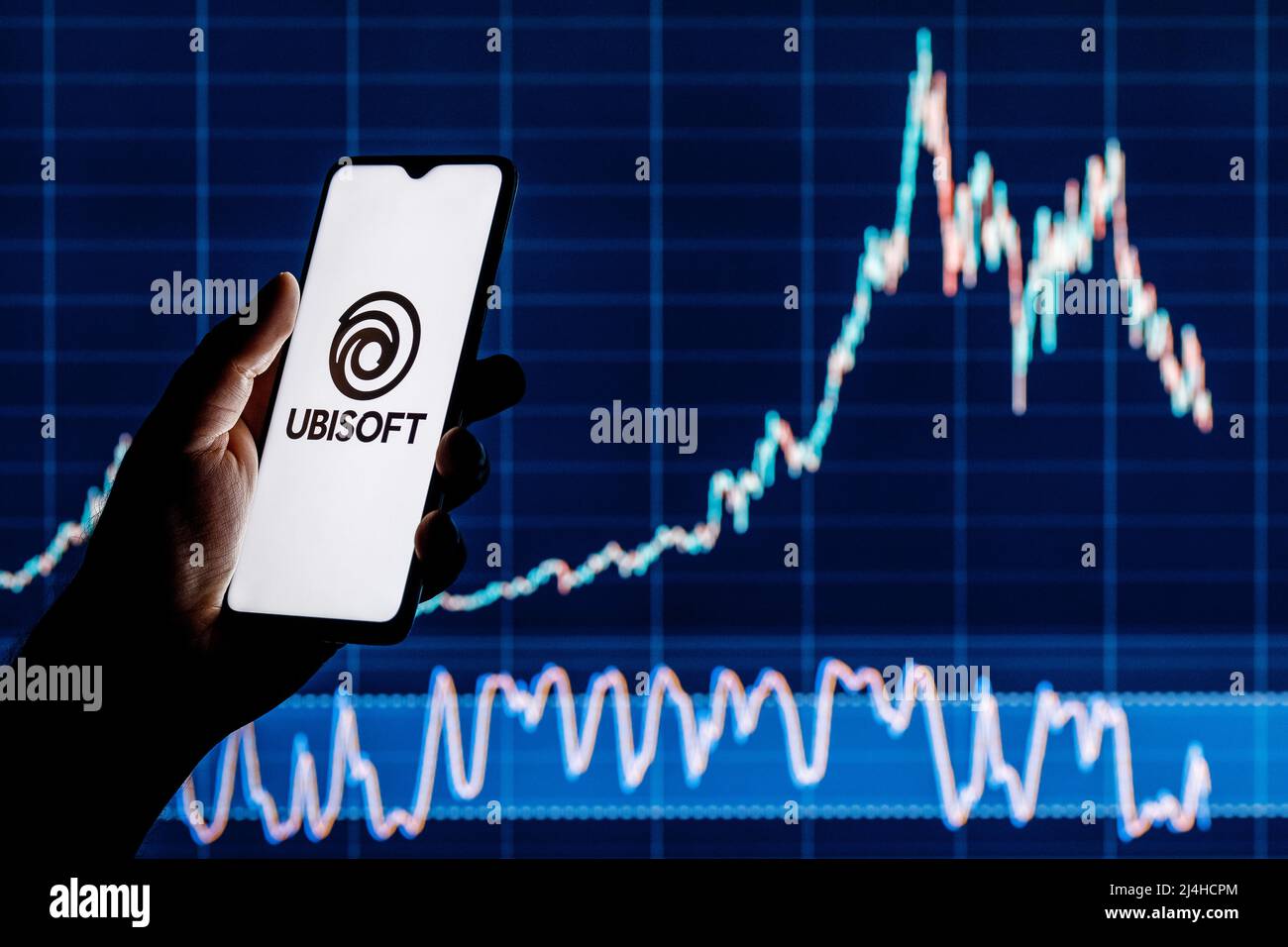 Ubisoft is French video game company. Smartphone with Ubisoft logo in hand. Stock chart on background. Stock Photo
