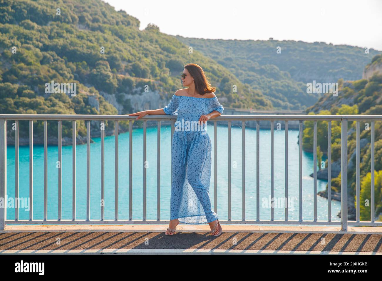 The beautiful girl in a blue dress and sunglasses poses on the bridge ...