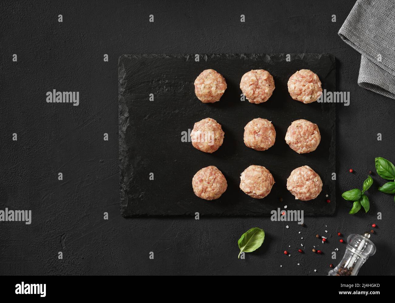 Raw meatballs with basil. Black background. Top view Stock Photo
