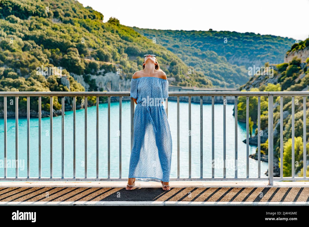 The beautiful girl in a blue dress and sunglasses poses on the bridge ...
