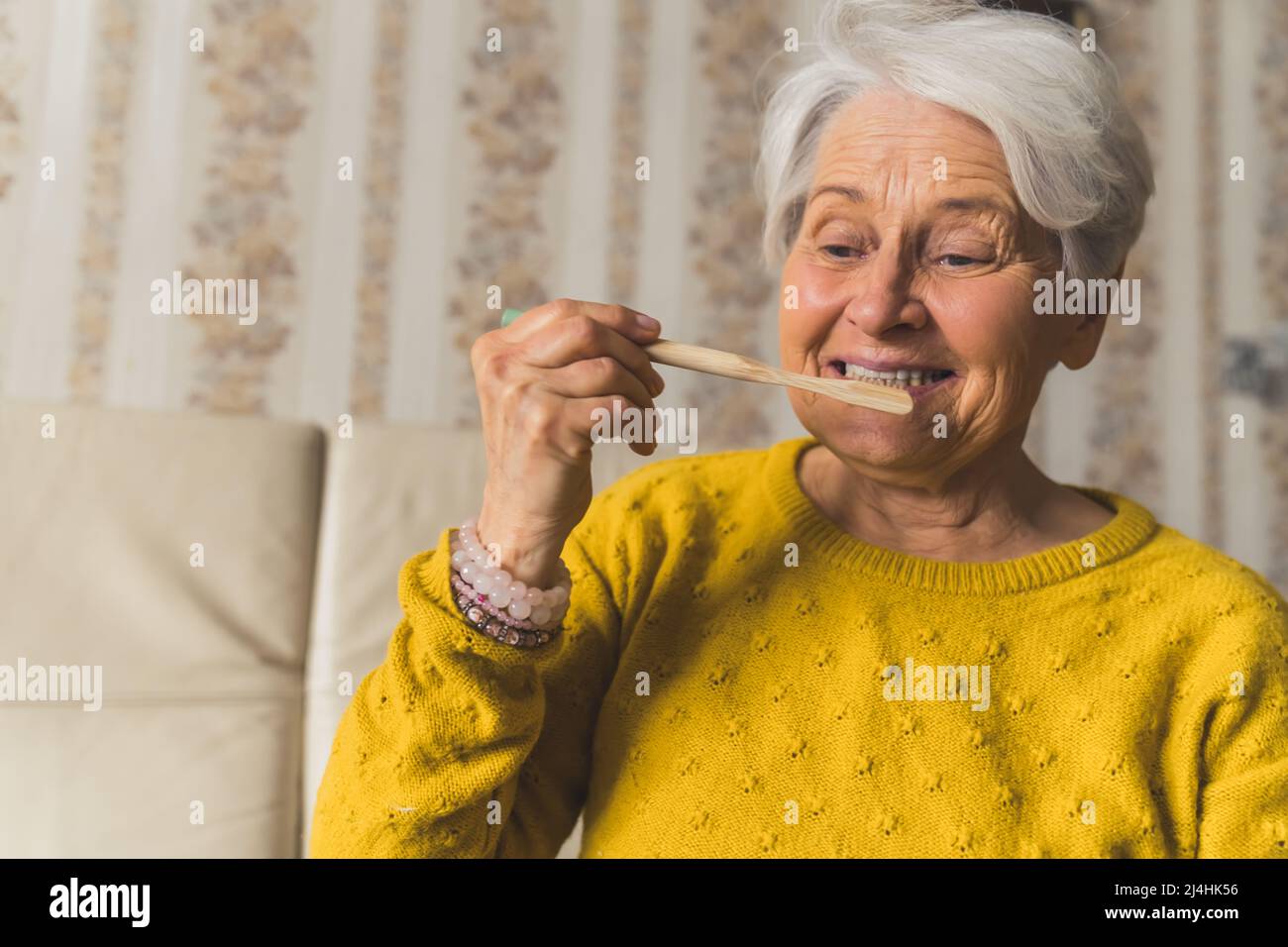 European elderly short-haired senior lady holding ecological bamboo toothbrush and brushing her teeth. The importance of hygiene. . High quality photo Stock Photo