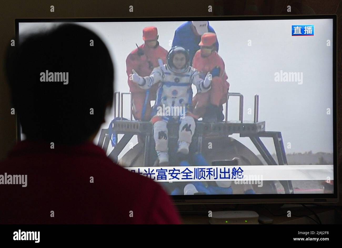 A woman watches a live TV broadcast of the successful landing of the Shenzhou XIII re-entry module with the astronaut Ye Guangfu on the TV screen. After orbiting Earth for six months, the three crew members of China's Shenzhou XIII mission departed from the Tiangong space station. They returned to the mother planet on Saturday morning, finishing the nation's longest human-crewed spaceflight. Major General Zhai Zhigang, the mission commander, Senior Colonel Wang Yaping, and Senior Colonel Ye Guangfu breathed fresh air for the first time after the half-year space journey as ground recovery perso Stock Photo