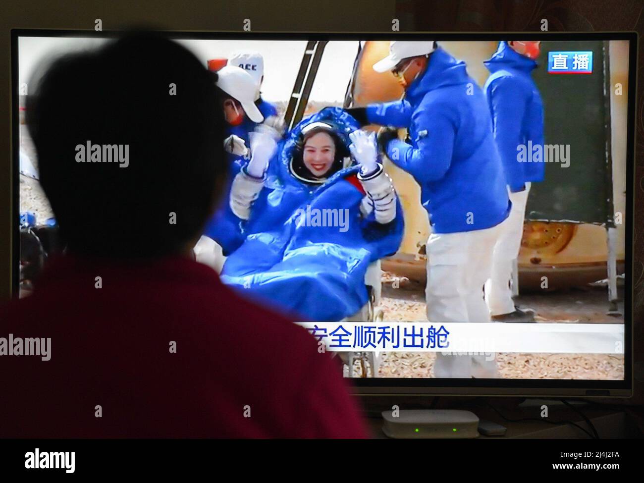 A woman watches a live TV broadcast of the successful landing of the Shenzhou XIII re-entry module with the astronaut Wang Yaping on the TV screen. After orbiting Earth for six months, the three crew members of China's Shenzhou XIII mission departed from the Tiangong space station. They returned to the mother planet on Saturday morning, finishing the nation's longest human-crewed spaceflight. Major General Zhai Zhigang, the mission commander, Senior Colonel Wang Yaping, and Senior Colonel Ye Guangfu breathed fresh air for the first time after the half-year space journey as ground recovery pers Stock Photo