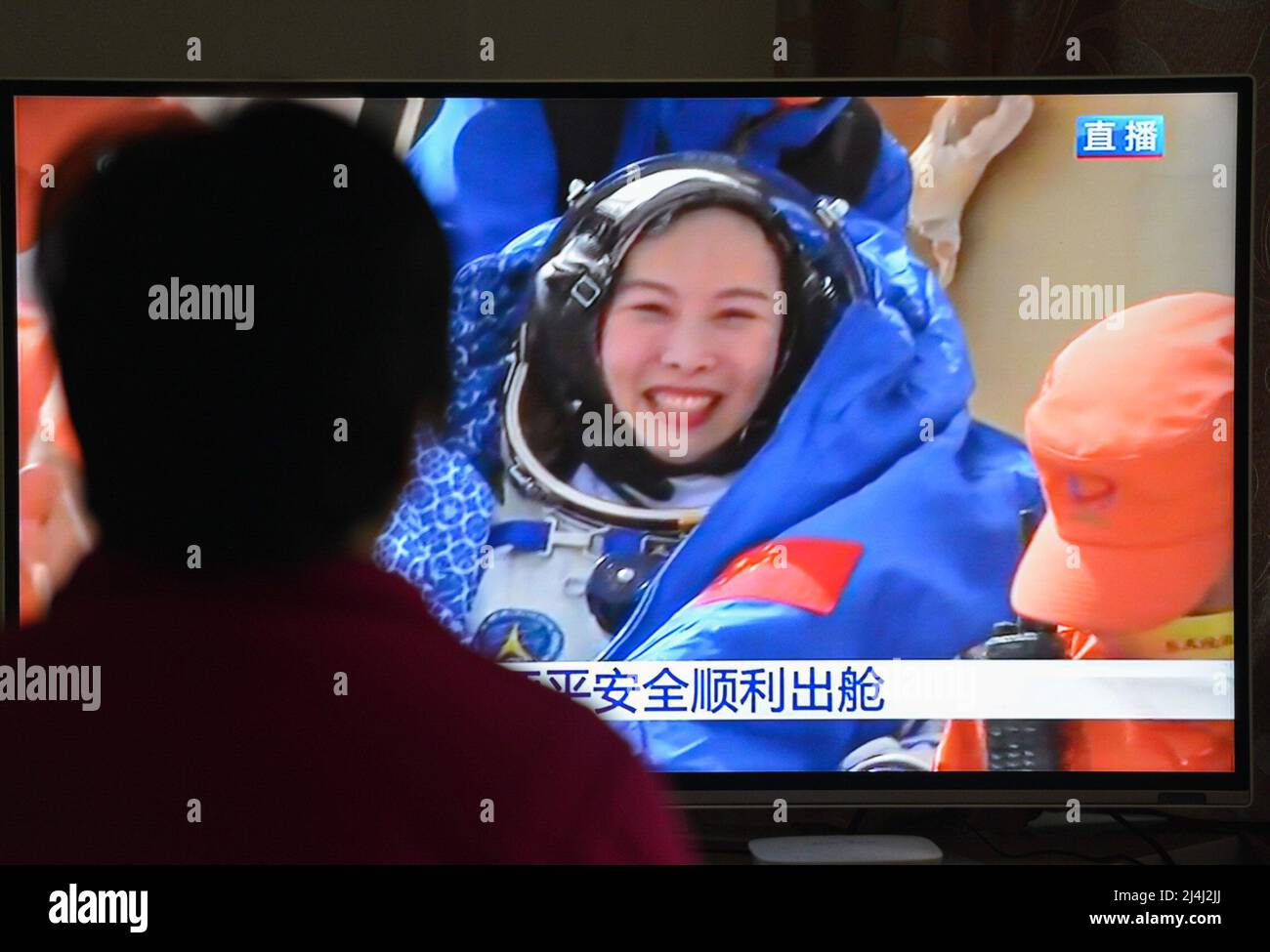 A woman watches a live TV broadcast of the successful landing of the Shenzhou XIII re-entry module with the astronaut Wang Yaping in the background. After orbiting Earth for six months, the three crew members of China's Shenzhou XIII mission departed from the Tiangong space station. They returned to the mother planet on Saturday morning, finishing the nation's longest human-crewed spaceflight. Major General Zhai Zhigang, the mission commander, Senior Colonel Wang Yaping, and Senior Colonel Ye Guangfu breathed fresh air for the first time after the half-year space journey as ground recovery per Stock Photo