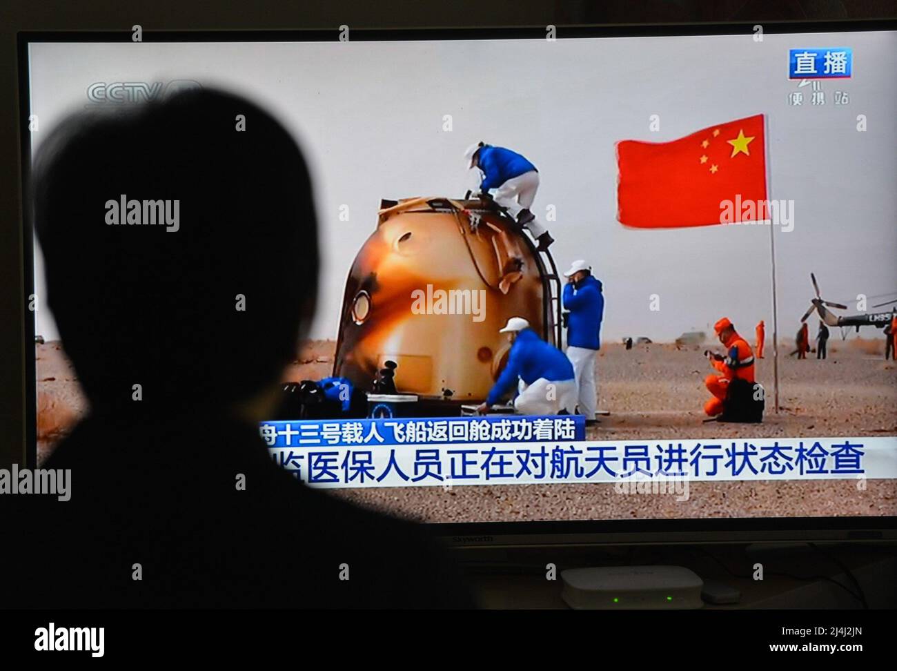 A woman watches a live TV broadcast of the successful landing of the Shenzhou XIII re-entry module. After orbiting Earth for six months, the three crew members of China's Shenzhou XIII mission departed from the Tiangong space station. They returned to the mother planet on Saturday morning, finishing the nation's longest human-crewed spaceflight. Major General Zhai Zhigang, the mission commander, Senior Colonel Wang Yaping, and Senior Colonel Ye Guangfu breathed fresh air for the first time after the half-year space journey as ground recovery personnel opened the hatch of their re-entry capsule Stock Photo