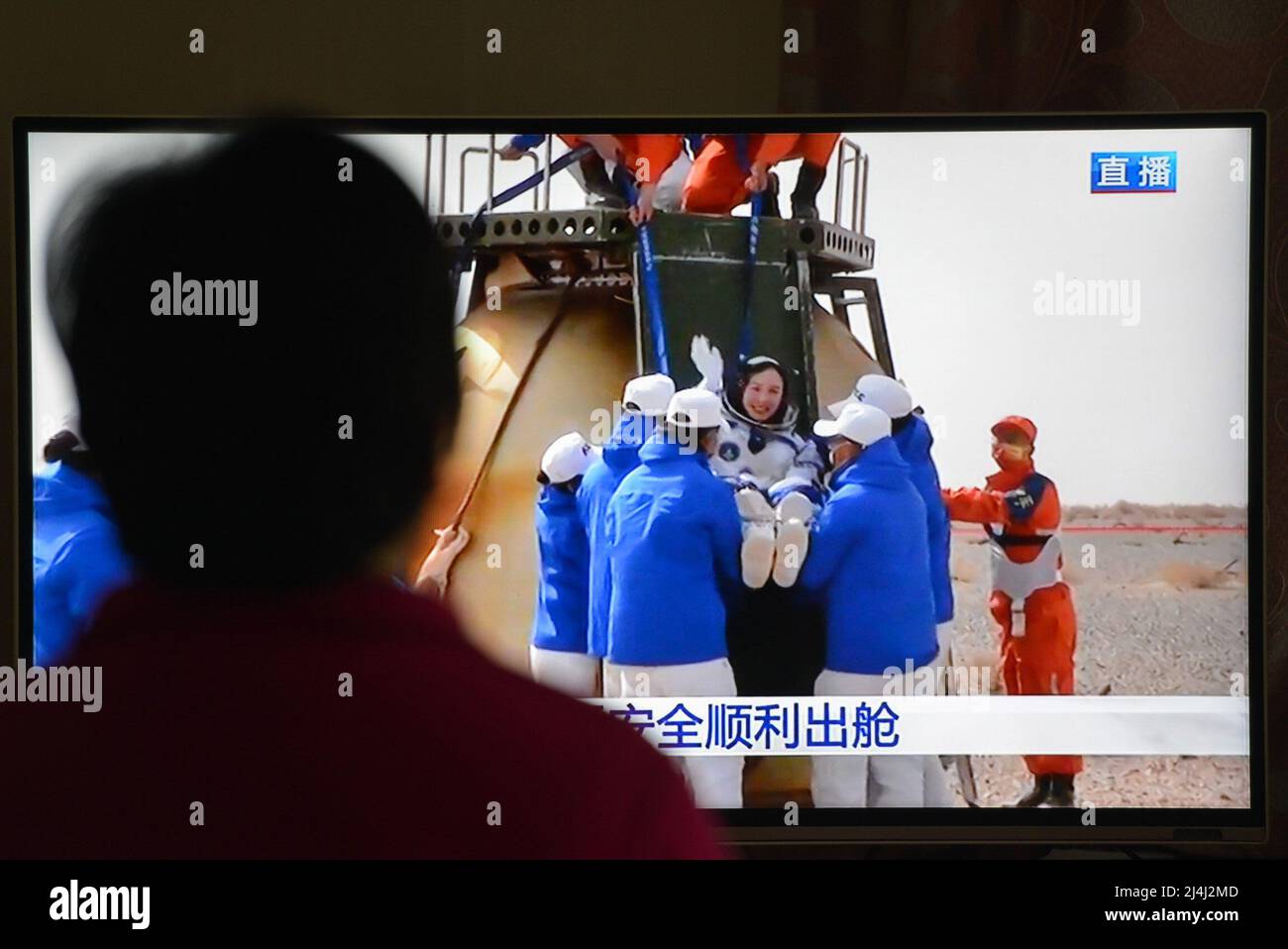 A woman watches a live TV broadcast of the successful landing of the Shenzhou XIII re-entry module with the astronaut Wang Yaping on the TV screen. After orbiting Earth for six months, the three crew members of China's Shenzhou XIII mission departed from the Tiangong space station. They returned to the mother planet on Saturday morning, finishing the nation's longest human-crewed spaceflight. Major General Zhai Zhigang, the mission commander, Senior Colonel Wang Yaping, and Senior Colonel Ye Guangfu breathed fresh air for the first time after the half-year space journey as ground recovery pers Stock Photo
