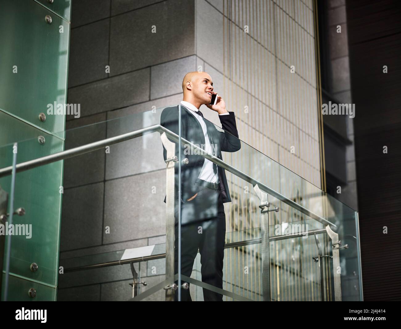 young latino corporate business man standing on top of stairs making a call using cellphone in modern office building Stock Photo
