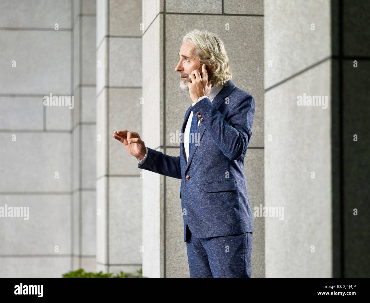 caucasian senior corporate executive standing in lobby of modern building talking on mobile phone. Stock Photo