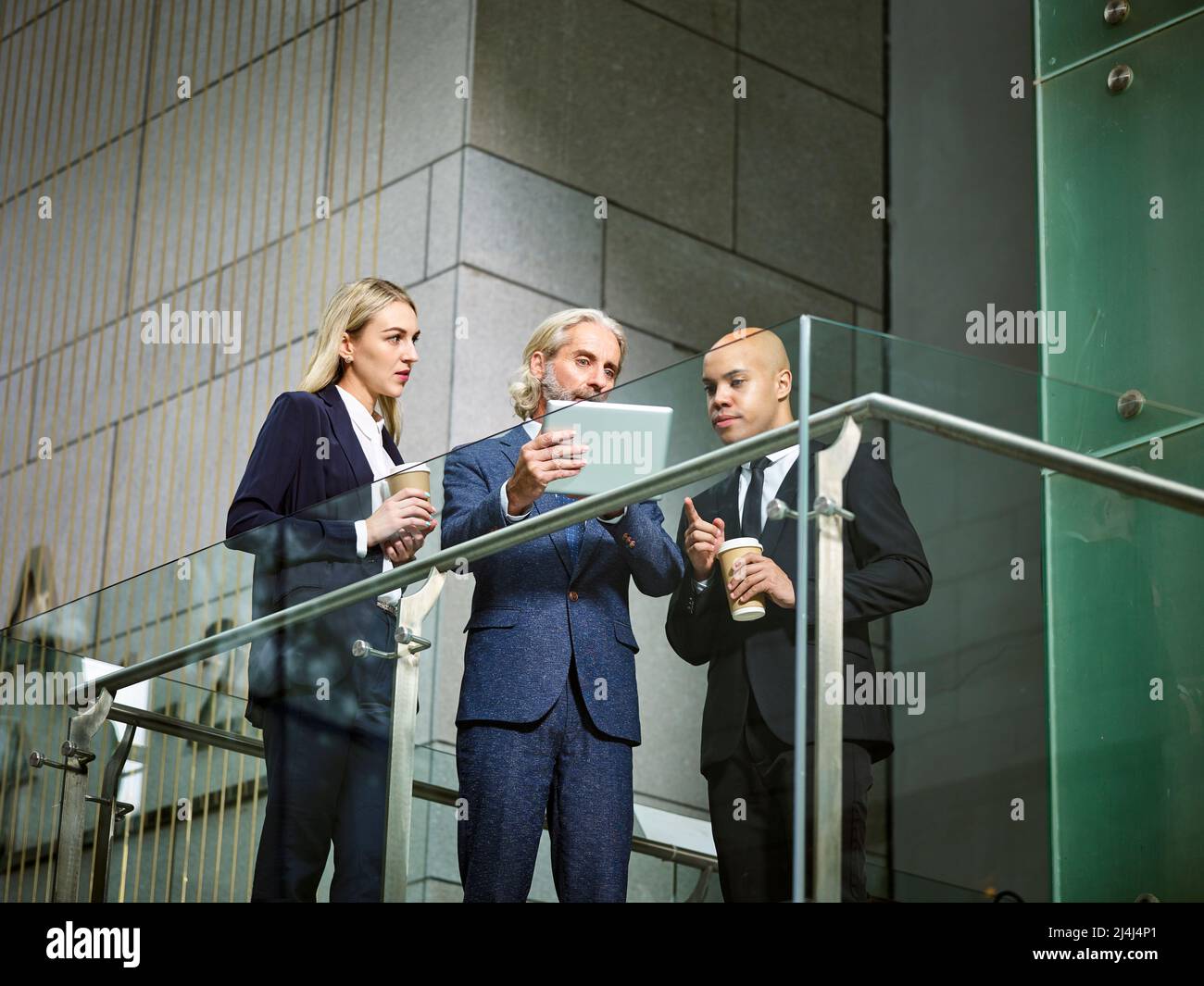 multinational and multiethnic corporate people discussing business using digital tablet in modern office building, low angle view. Stock Photo