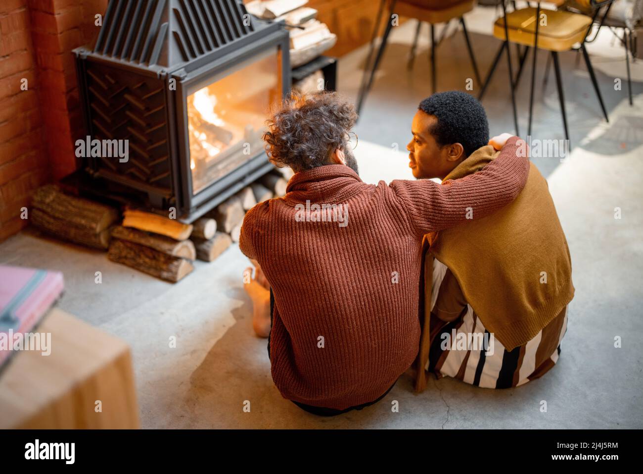Two men sitting together by the burning fireplace at cozy home Stock