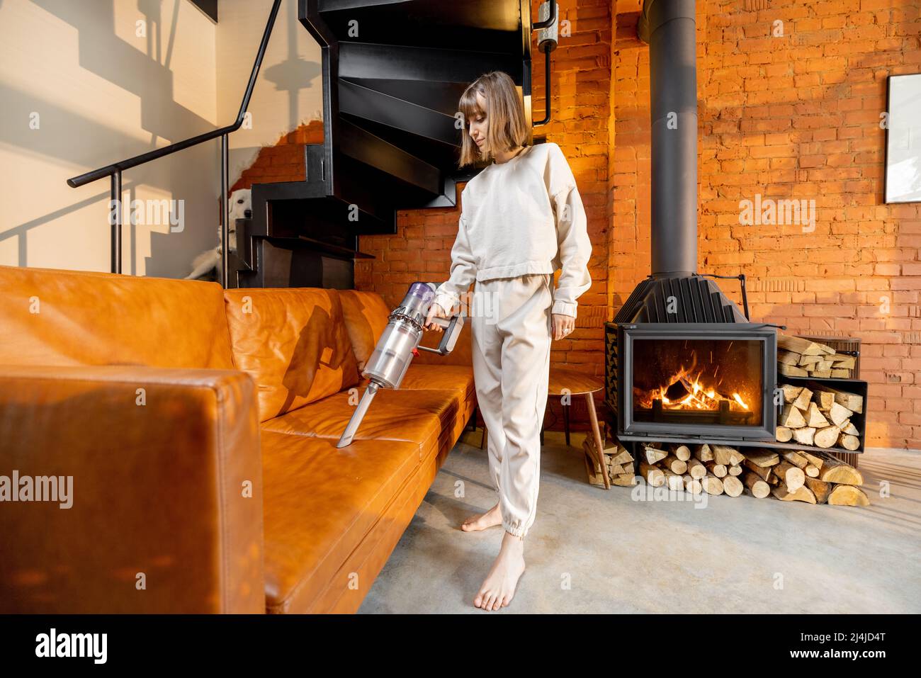 Woman vacuuming couch with wireless handheld vacuum cleaner Stock Photo