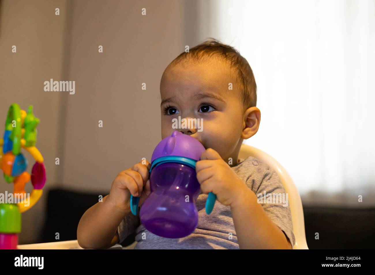 Caucasian child, boy, 3-4 year old, sitting on settee, holding in hand a  plastic cup and drinking from it while watching something in front Stock  Photo - Alamy