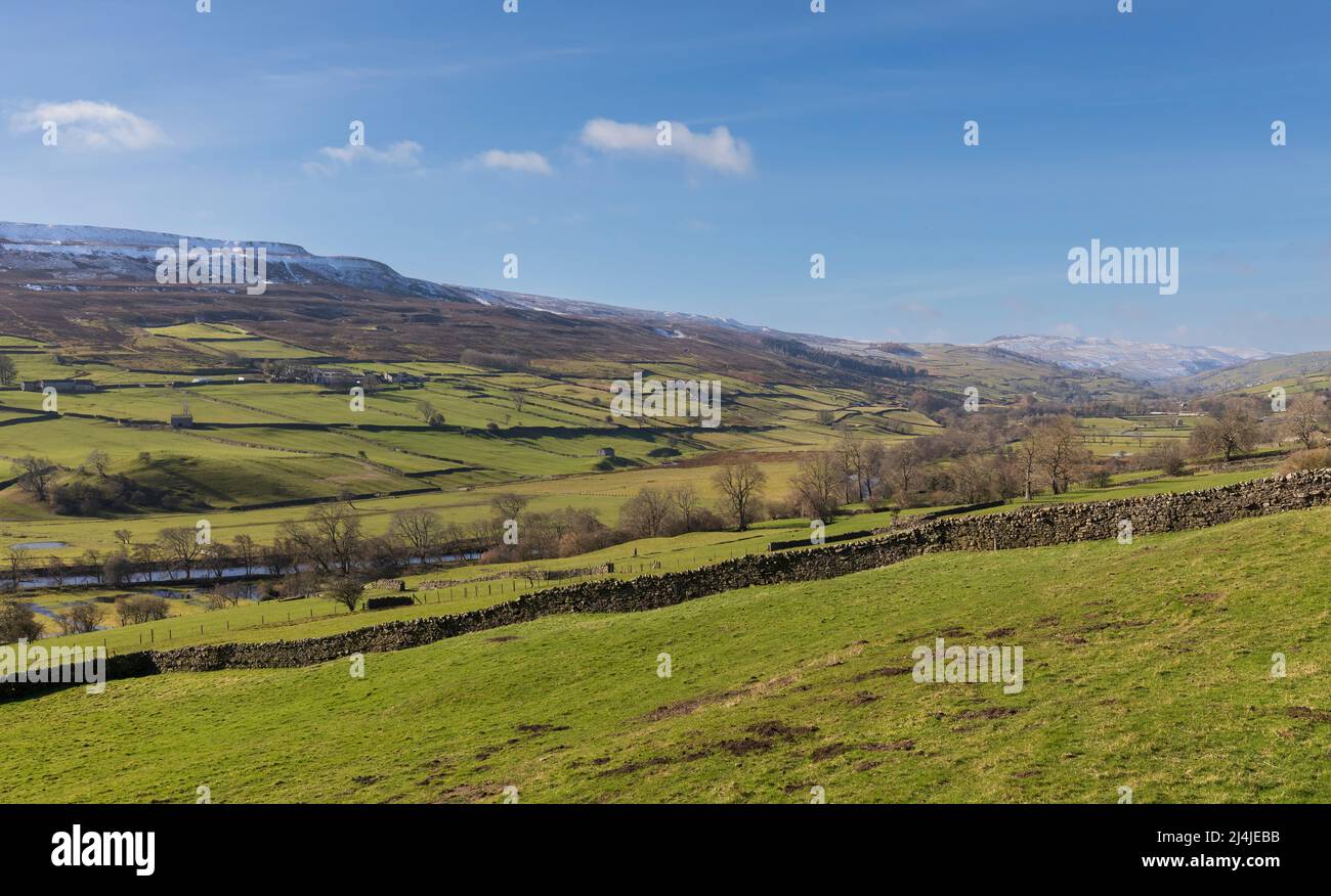 Swaledale, Yorkshire Dales National Park, Snow covered hills above a patchwork of dry stone wall lined fields and pastures with iconic stone barns. Stock Photo