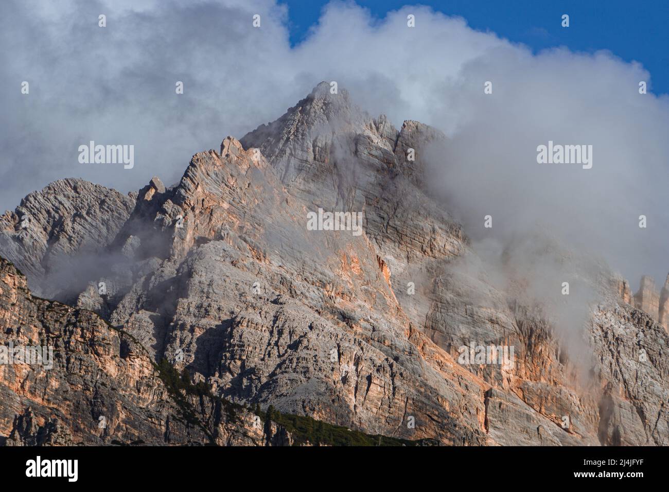 The peaks of the Dolomites, with the lights of the sunset, immersed in the fog, near the town of Cortina d'Ampezzo, Italy - October 2021. Stock Photo