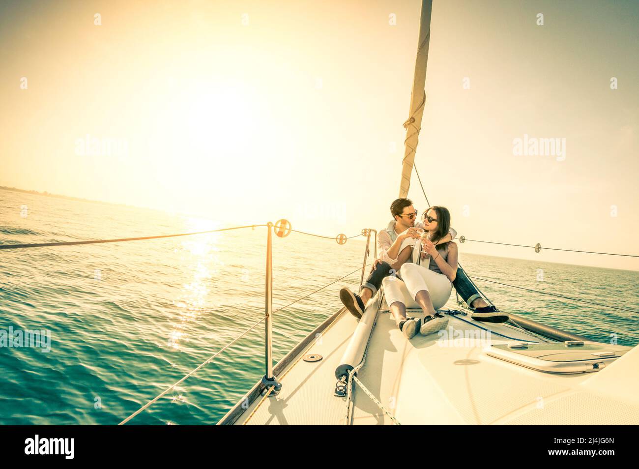 Young couple in love on sail boat with champagne at sunset - Happy exclusive alternative lifestye concept  - Soft focus due to backlight Stock Photo
