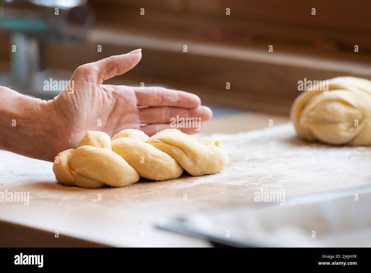 Lady's hand forms a handmade easter braid in the kitchen from sweet yeast dough Stock Photo