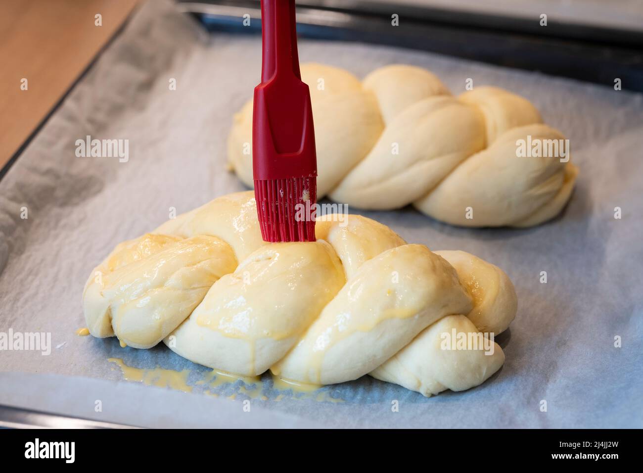 woman with brush spreads easter braid with eggs milk glaze on baking sheet Stock Photo