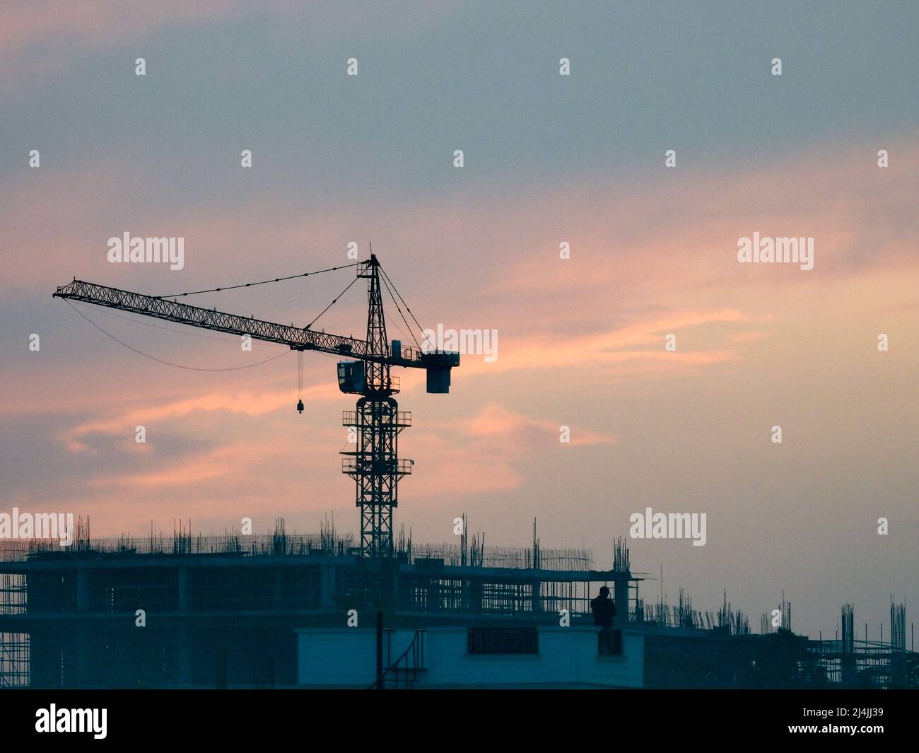 A wide-angle shot of a big heavy crane working on a construction site in the evening. Stock Photo