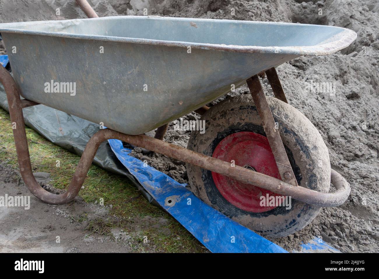 A metal wheelbarrow next to a pile of yellow sand, ready to use for the work Stock Photo