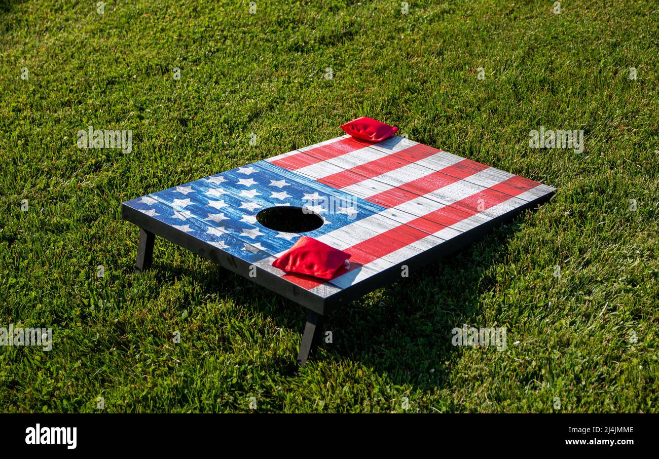 Two red bean bags on a cornhole game that is painted as an American flag on a green grass field. Stock Photo