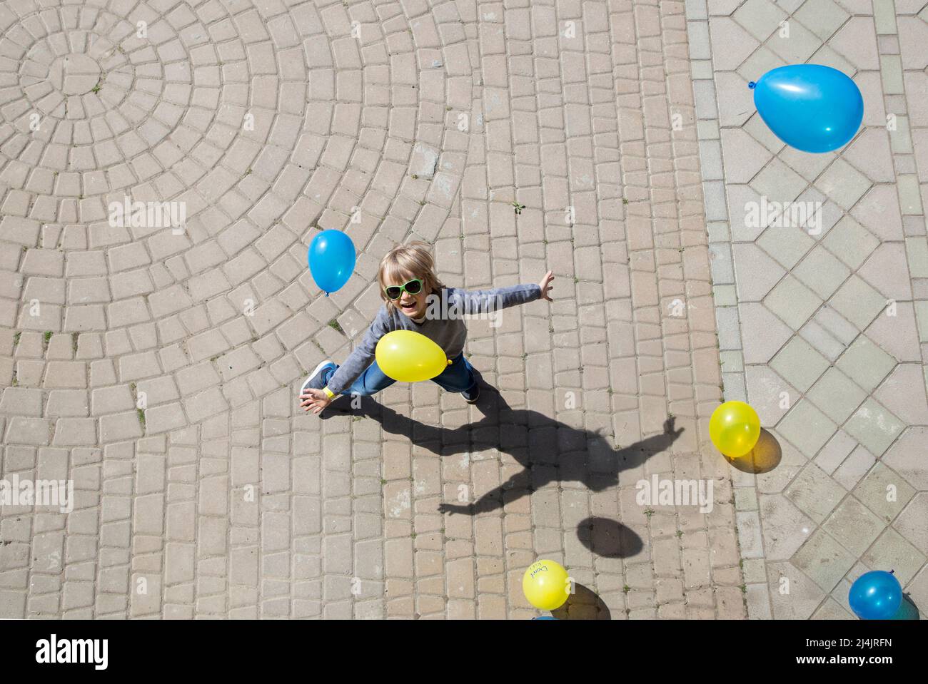cheerful preschool boy catches a lot of yellow and blue balls falling from above on him. Ukrainian children against the war. happy childhood, have fun Stock Photo