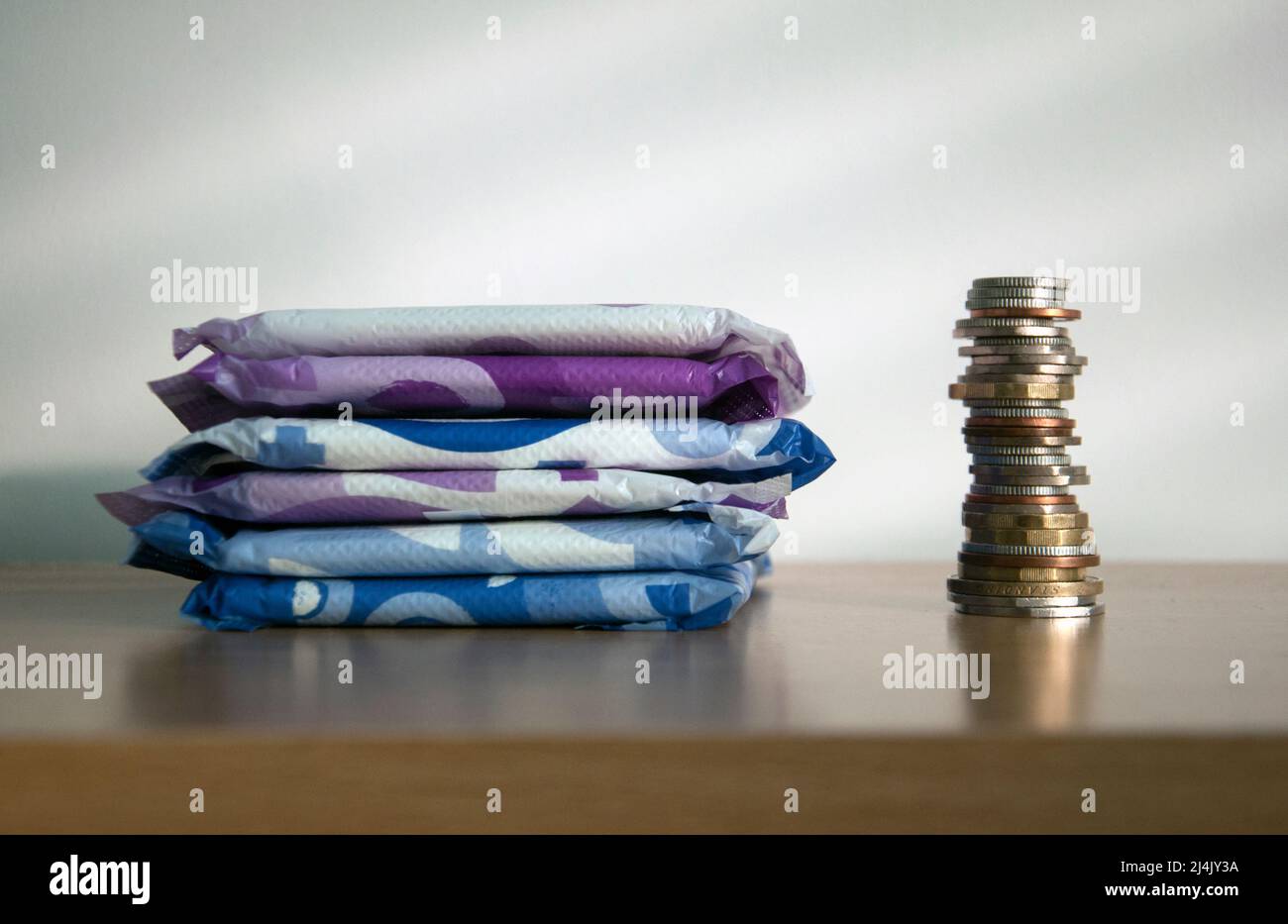 A stack of sanitary towels next to a taller stack of coins. Illustrating period poverty and unaffordability of sanitary materials for many women world Stock Photo